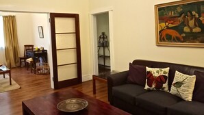 Uma sala de estar com um sofá escuro, uma mesa de centro de madeira e uma pintura na parede.