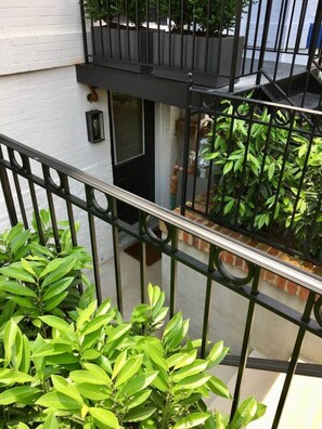 Un balcon avec une balustrade en métal, des plantes en pot et un bâtiment blanc en arrière-plan.