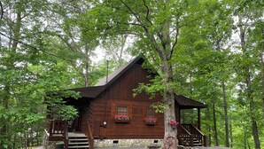 A rustic wooden cabin with a stone foundation, surrounded by lush greenery. - A+ Location 2 mi Pigeon Forge Pkwy,Not up Mtn, Hottub, Quiet,Private,SUPER CLEAN (Sevierville)