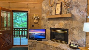 A cozy living room with a stone fireplace, a television, and a wooden door leading to a balcony. - A+ Location 2 mi Pigeon Forge Pkwy,Not up Mtn, Hottub, Quiet,Private,SUPER CLEAN (Sevierville)