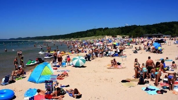 A crowded beach with people sunbathing, swimming, and using beach umbrellas. - Hilltop Cottage in Pentwater Village (Pentwater)