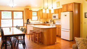 A spacious kitchen with wooden cabinets, a central island, bar stools, and a refrigerator. - Hilltop Cottage in Pentwater Village (Pentwater)