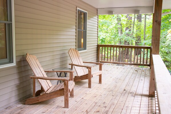 Eine Holzterrasse mit zwei Adirondack-Stühlen und einem kleinen Tisch.