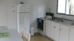 A compact kitchen with a refrigerator, stove, sink, and a small trash bin.
