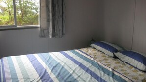 A bedroom with a striped bedspread, a floral pillow, and a window with curtains.