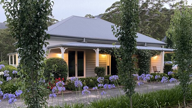 A two-story house with a gabled roof, a front porch, and a well-maintained garden with purple flowers and green shrubs. - Marden Meadows - Luxury home in Kangaroo Valley (Kangaroo Valley)