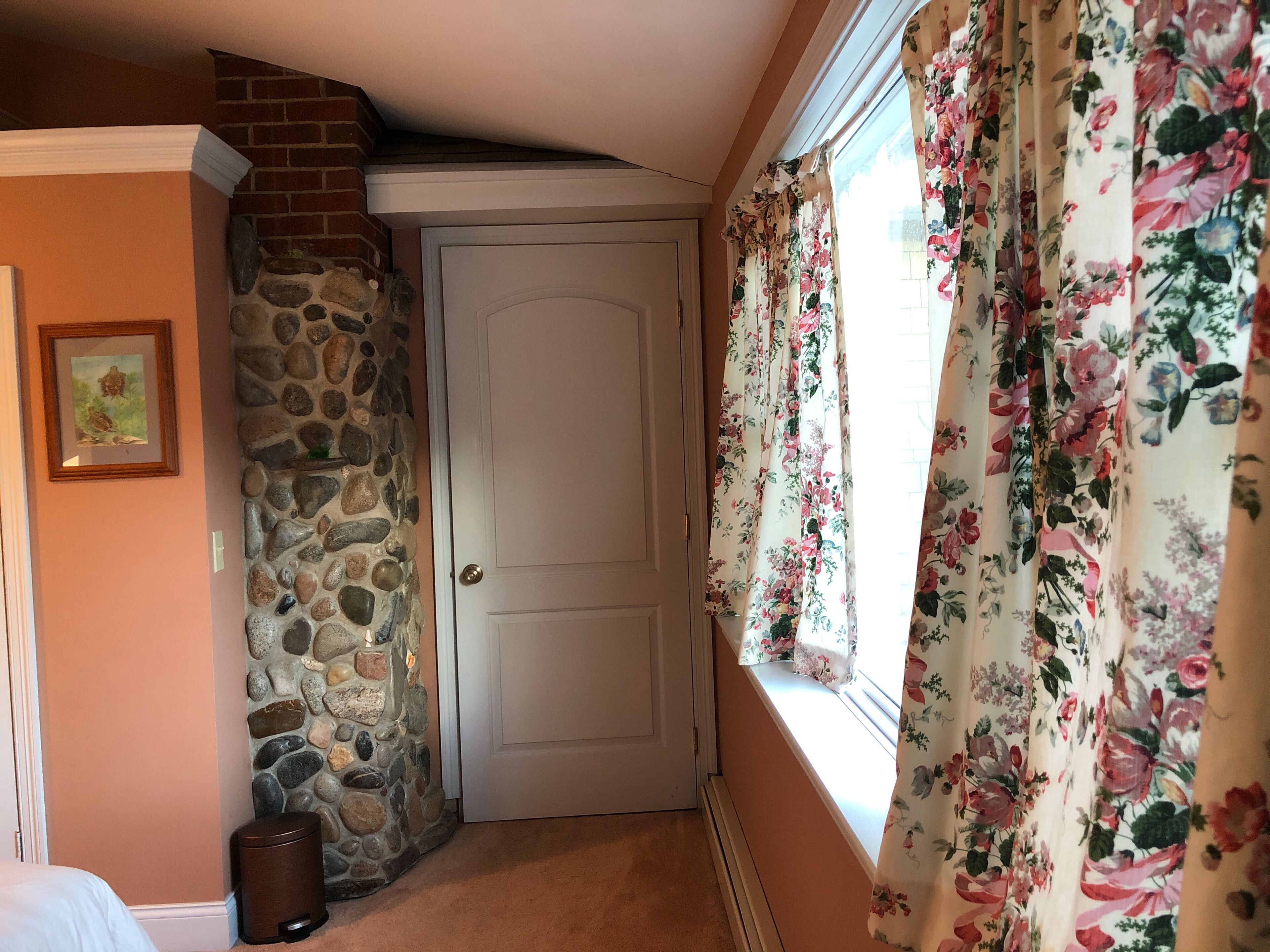 Une pièce avec un mur en pierre, une porte blanche et des rideaux à motifs floraux.