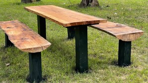 Een houten picknicktafel met bankjes in een grasveld nabij een rivier.