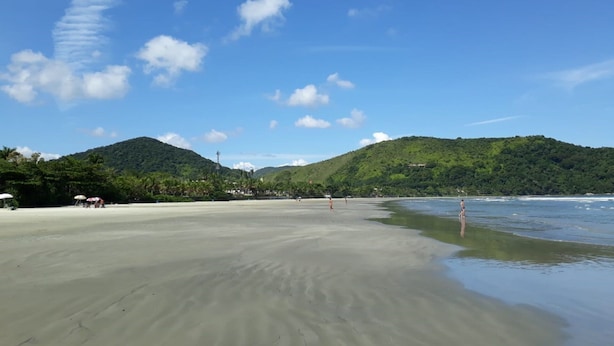 A beach with a sandy shore, clear blue sky, and green hills in the background.