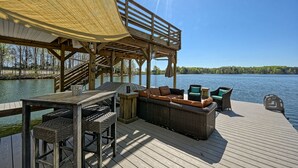 Une terrasse en bois avec des meubles d’extérieur, un espace salon couvert et une vue sur un lac.