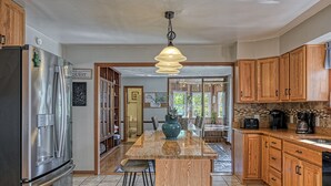 Une cuisine avec des meubles de rangement en bois, un réfrigérateur en acier inoxydable, un îlot central avec des tabourets et un luminaire suspendu.
