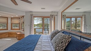 Une chambre avec un grand lit, un ventilateur de plafond, une vue sur un lac par la fenêtre et un balcon avec une balustrade.