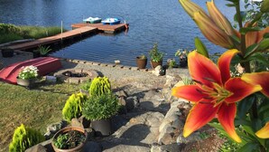 A lakeside patio with potted plants, a dock with boats, and a view of a forested area.