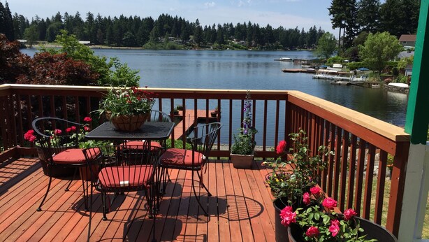 A wooden deck with a table and chairs, surrounded by potted plants and flowers.