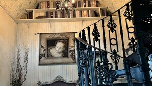 Eine Treppe mit aufwendiger schwarzer Metallreling, einem Chandelier und einem Bücherregal voller Bücher.