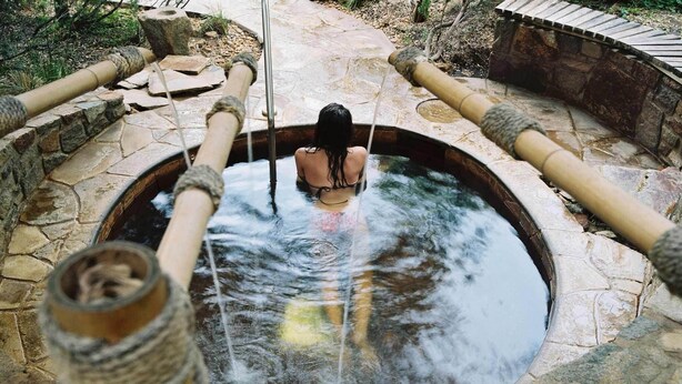Ein Steine-Thermalbad mit einer Person in der Mitte, umgeben von Steinmauern und Bambusrohren.
