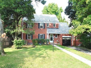 A two-story brick house with a front garage, surrounded by a well-maintained lawn and trees.