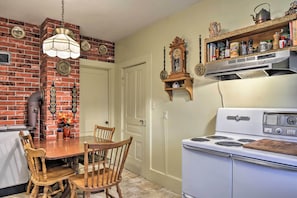 Una cocina con pared de ladrillo, estufa blanca, sillas de madera y una lámpara colgante.
