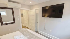 Une chambre d’hôtel avec un grand lit, un téléviseur à écran plat fixé au mur, un miroir et une porte donnant sur une autre pièce.