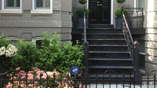 Un bâtiment à deux étages avec une porte d’entrée noire, des fenêtres à cadre blanc et une façade en briques.