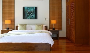 A bedroom with a wooden bed, two bedside lamps, a peacock-themed painting, and a wooden wardrobe.