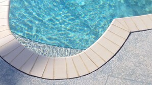 Piscina com água cristalina, borda e deck revestidos em azulejo.