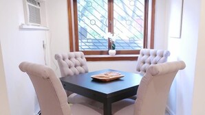Un comedor con una mesa de madera oscura y cuatro sillas tapizadas, una ventana con vistas y una pequeña jarra blanca en el alféizar.