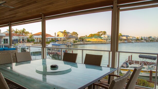 Una mesa con cubierta de vidrio y sillas de mimbre en una terraza con vista a un puerto deportivo con barcos y casas.
