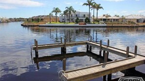 Una propiedad frente al agua, con muelle, palmeras y casas modernas al fondo.
