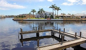 A waterfront property with a dock, palm trees, and modern houses in the background. - Waterside Canal Dreams (Mandurah)
