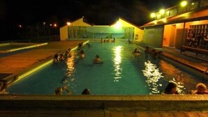 Zona de piscina por la noche con gente nadando y relajándose.