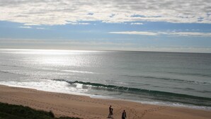 Une plage où l’on peut voir des empreintes de pas menant à l’eau, un ciel dégagé et une mer calme.