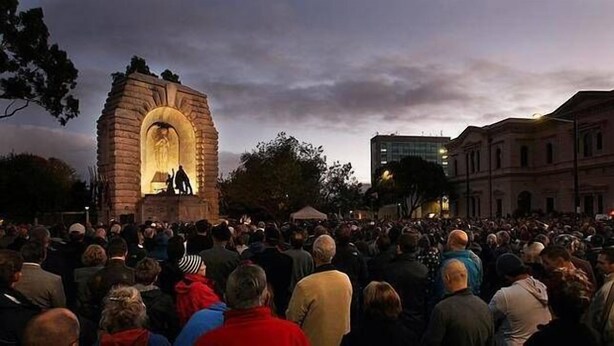 Una gran multitud s'ha reunit al voltant d'un monument de pedra amb una figura il·luminada a l'interior, envoltat d'edificis.