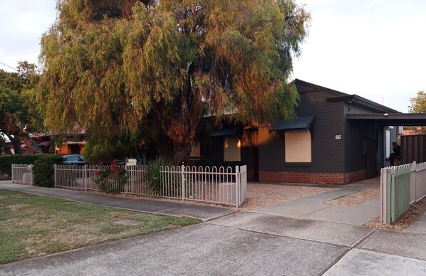 A modern two-story house with a dark exterior, a white picket fence, and a large tree in front.