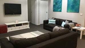 A living room with a dark brown sofa, a white entertainment unit, a flat-screen TV, and two abstract paintings on the wall. - Beach gemPhillip Island (sunderland bay)