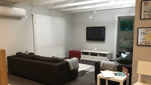 A modern living room with a dark sofa, a white TV stand, and a small table. - Beach gemPhillip Island (sunderland bay)