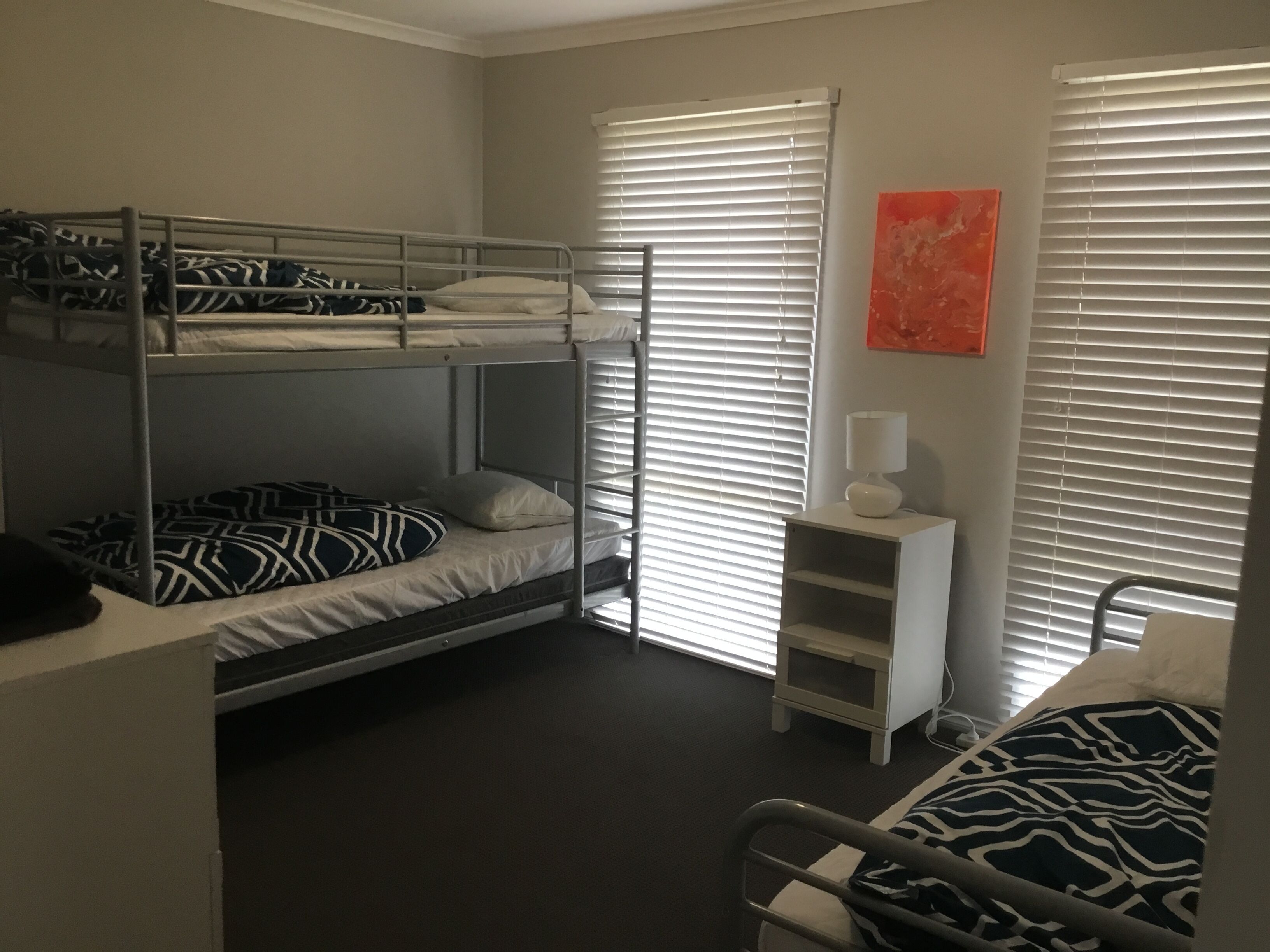 A bunk bed room with a small white nightstand and a lamp.