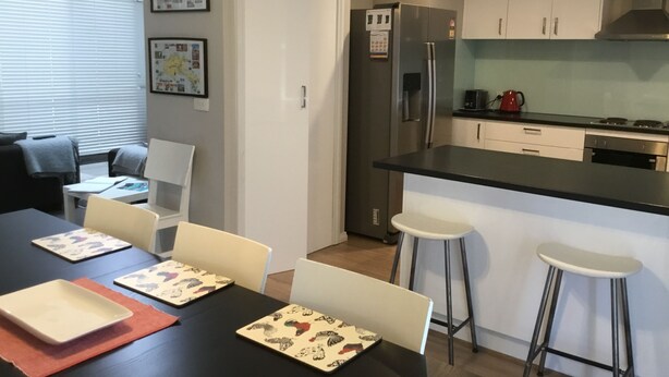 A compact kitchen with a refrigerator, stove, and bar stools. - Beach gemPhillip Island (sunderland bay)