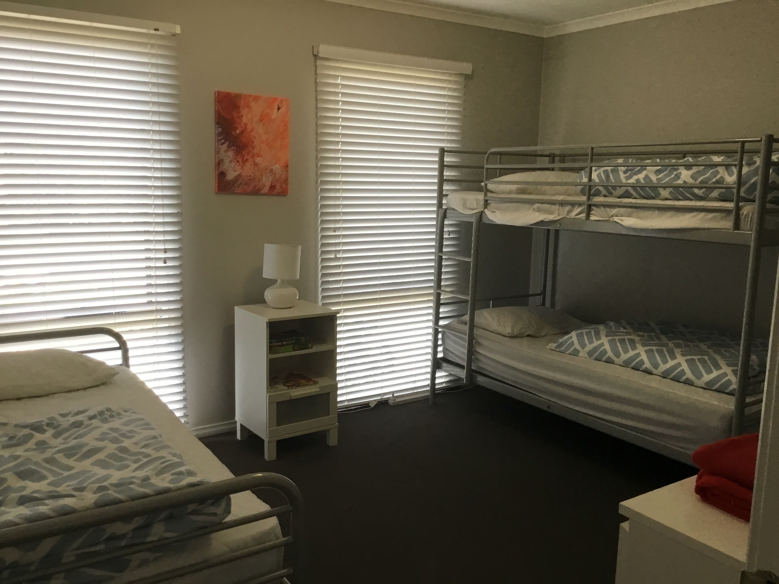 A room with bunk beds, a bedside table with a lamp, and a painting on the wall.