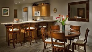 A modern kitchen with wooden cabinetry, a central island, and a dining area with wooden chairs and a round table. - Los Suenos Marina and Resort - Del Mar Luxury Condo 3 Br/2 Ba (Herradurra Beach Jaco)