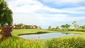 A golf course with a pond, palm trees, and houses in the background. - Los Suenos Marina and Resort - Del Mar Luxury Condo 3 Br/2 Ba (Herradurra Beach Jaco)