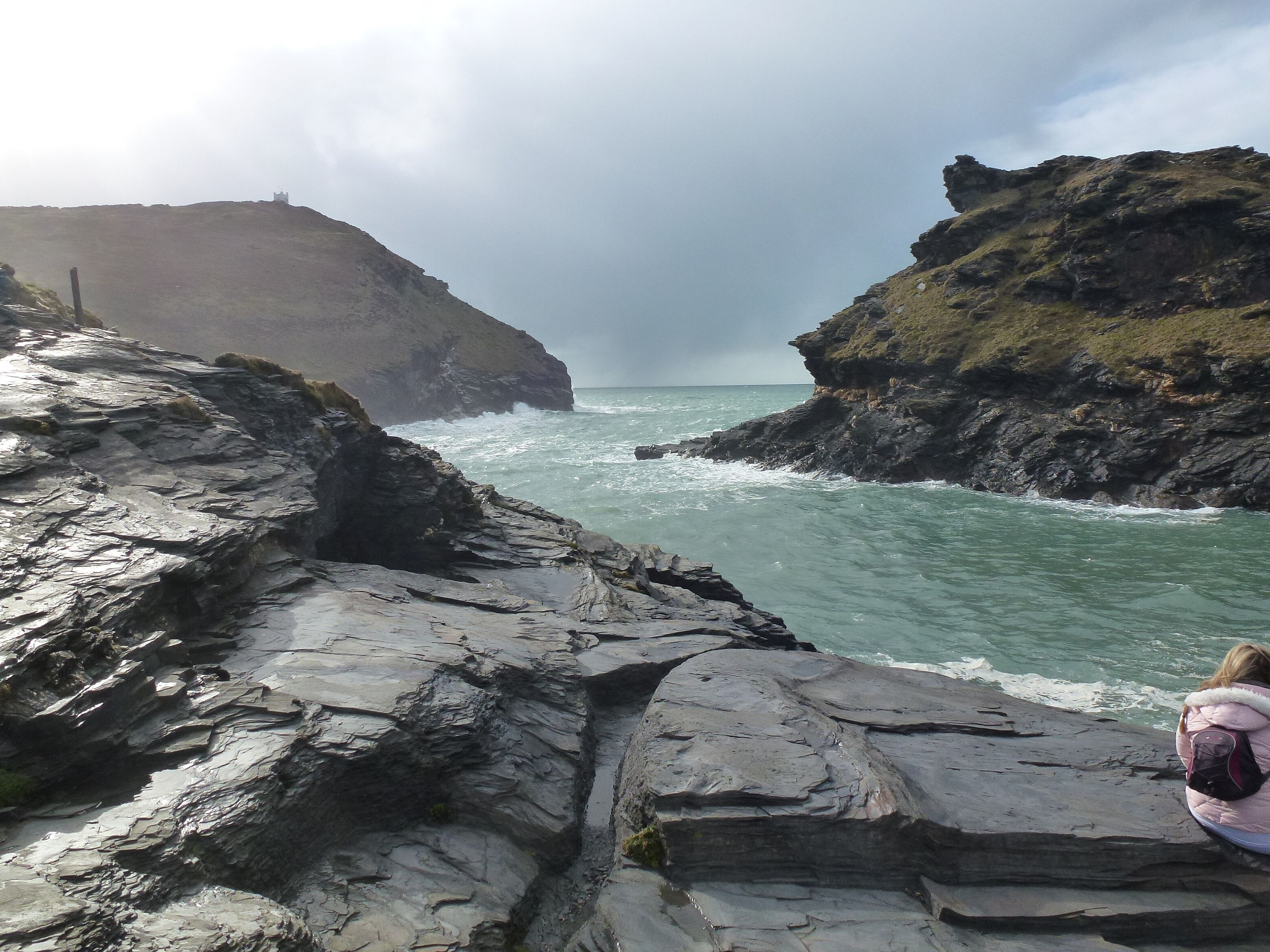 A rocky coastline with a person sitting on a ledge overlooking the sea.
