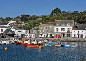 Un port où sont amarrés différents types de bateaux, des bâtiments abritant des boutiques et, au loin, une colline.