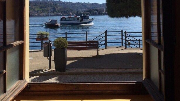 A view from a room with a large window overlooking a body of water with boats, a dock, and a hill in the background. - Pella: Pella, Lake of Orta: house on the Lake,fantastic view (Pella)
