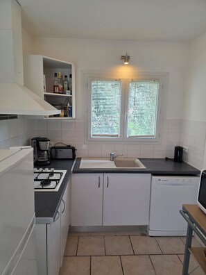 Cocina compacta con armarios blancos, estufa a gas, cafetera y lavavajillas.