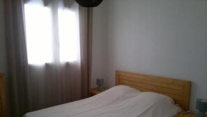 A bedroom with a single bed, a wooden headboard, a bedside table with a lamp, and a window with curtains.