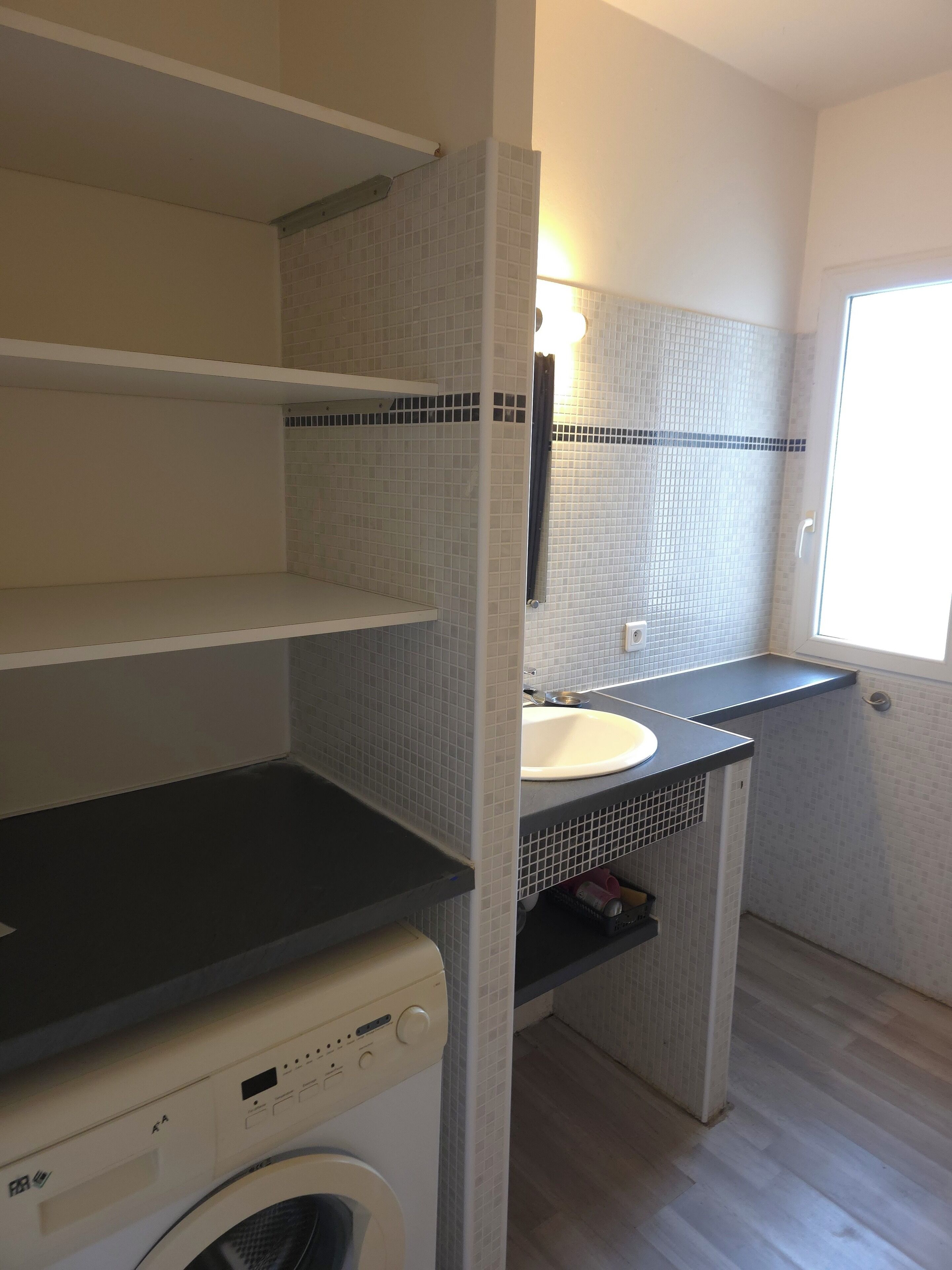 A compact bathroom with a washing machine, a sink, and a shower area.