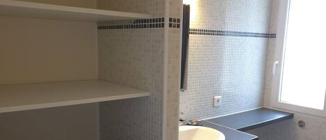 A compact bathroom with a washing machine, a sink, and a shower area.