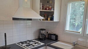 A kitchen with white cabinets, a gas stove, a coffee maker, and a window with blinds.