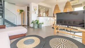 A modern living room with a sofa, TV, and two large woven rugs. There is a staircase to the left and a kitchen area in the background. - MAR COLONIA - Apartment with sea views in Colonia de Sant Jordi. Free WiFi (Ses Salines)